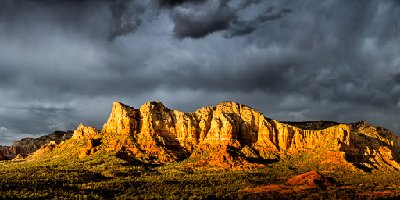 Sedona Splendor Courthouse Butte, Lee Mountain, Gibraltar Rock and Twin Buttes along Route 179 brightly lit at sunset under dark stormy skies in Sedona, AZ